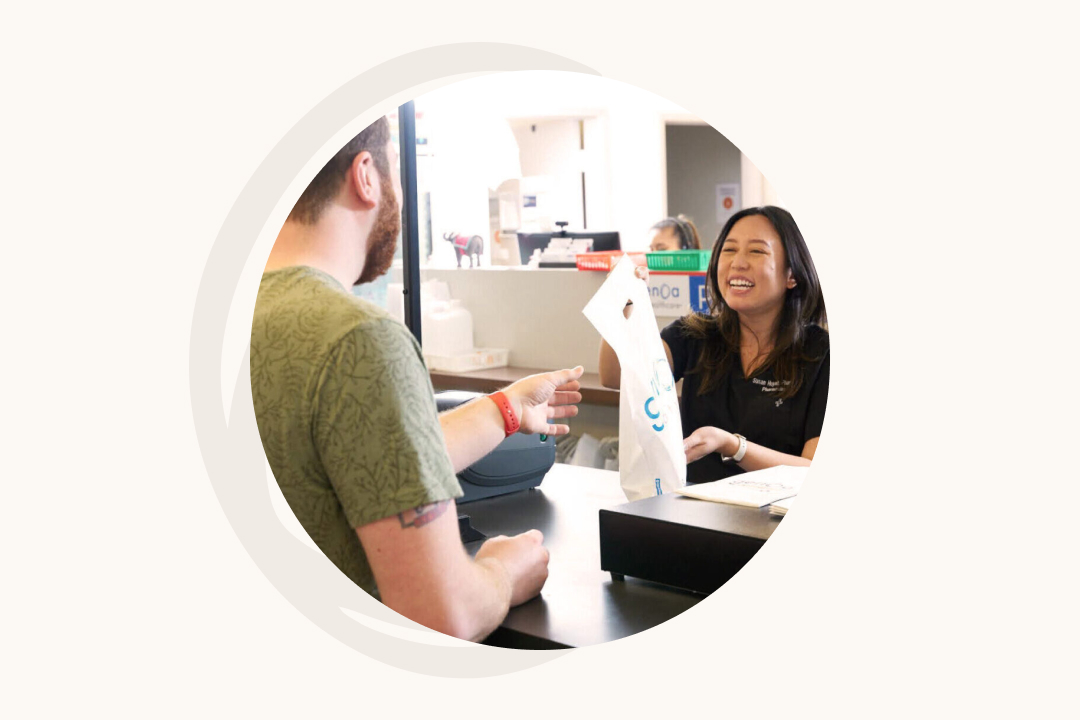 Genoa consumer stands at the pharmacy counter talking to a pharmacist who is handing her a pill bottle filled.